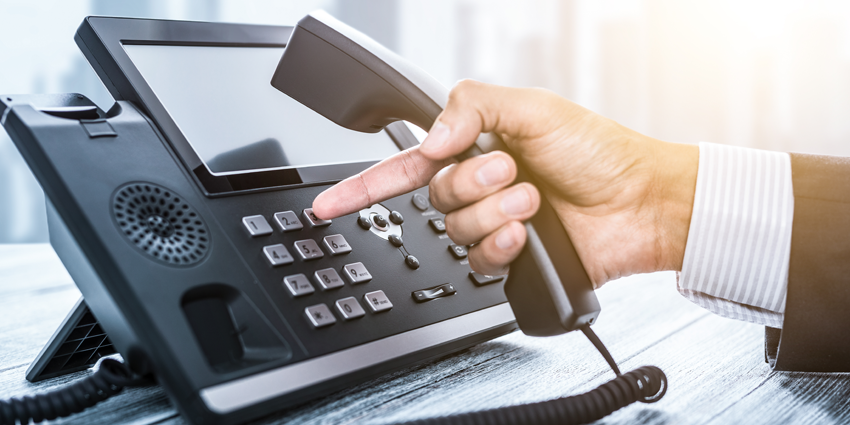 A hand holding a telephone handset above a business phone with a keypad.
