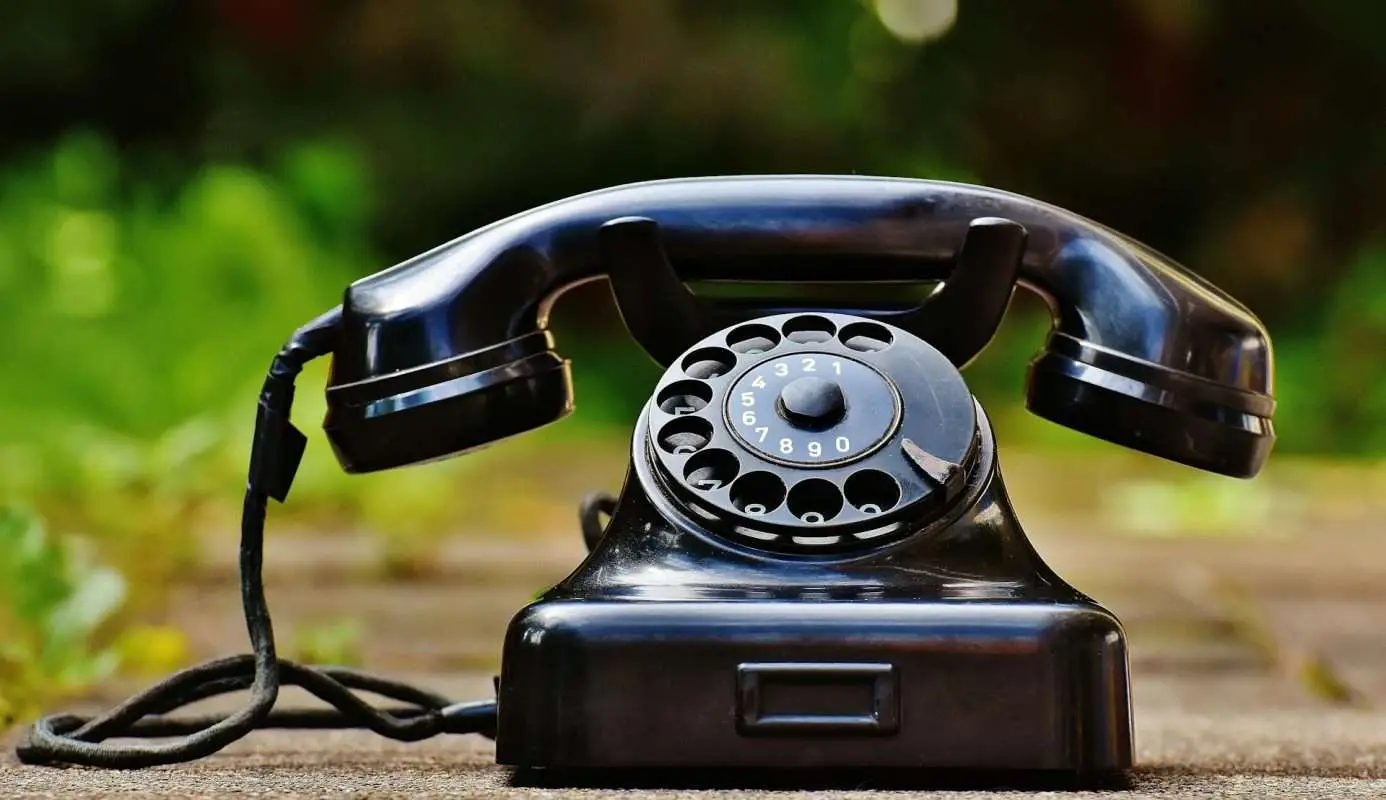 A vintage black rotary dial telephone with a circular dial and coiled cord.