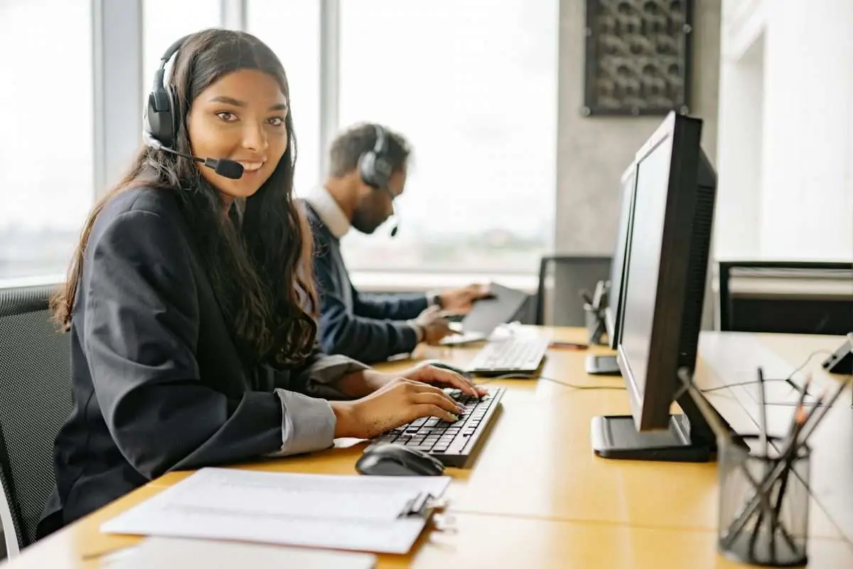 Two call center employees wearing headsets while working at their desks with computers.