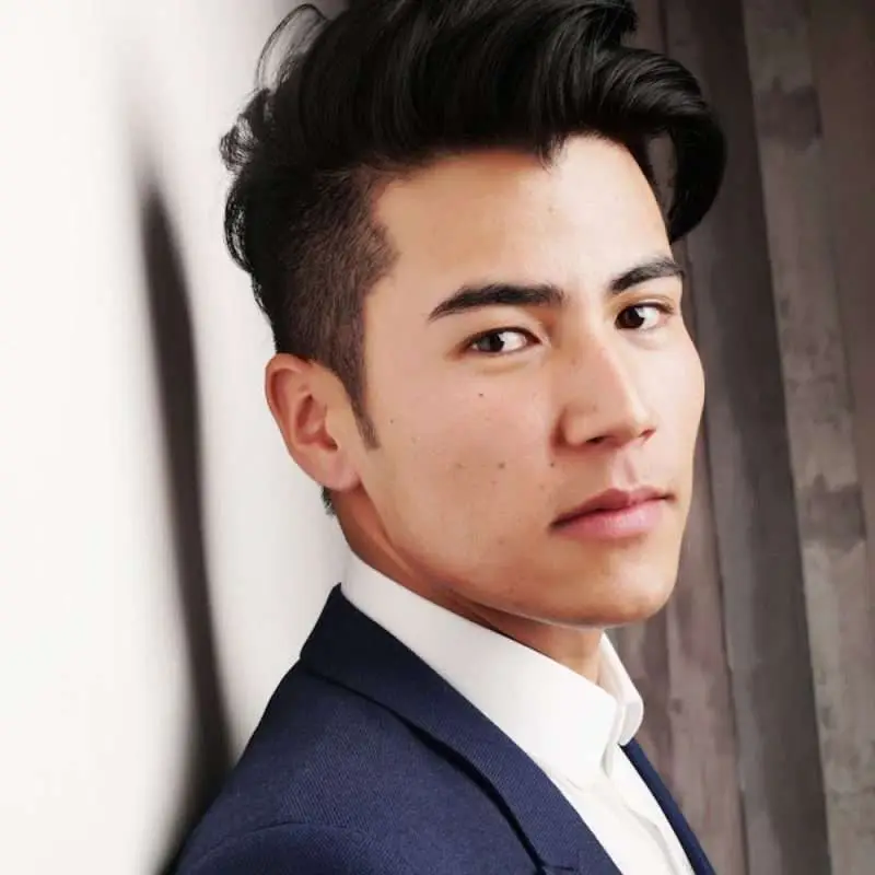 A young man with dark hair wearing a suit, looking directly at the camera with a neutral expression.